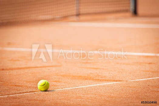 Picture of Yellow tennis ball on orange sand and white lines